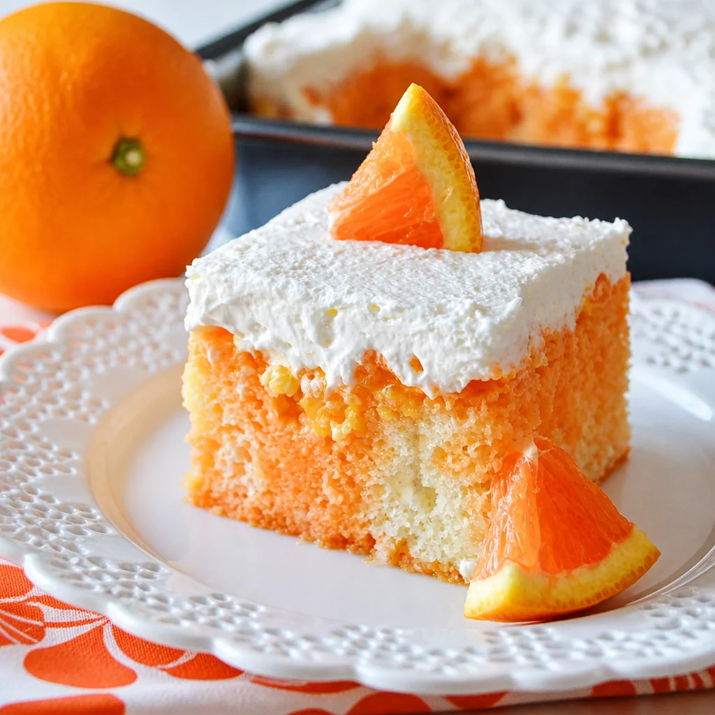 Slice of Orange Dreamsicle Poke Cake with orange jello and whipped cream topping.