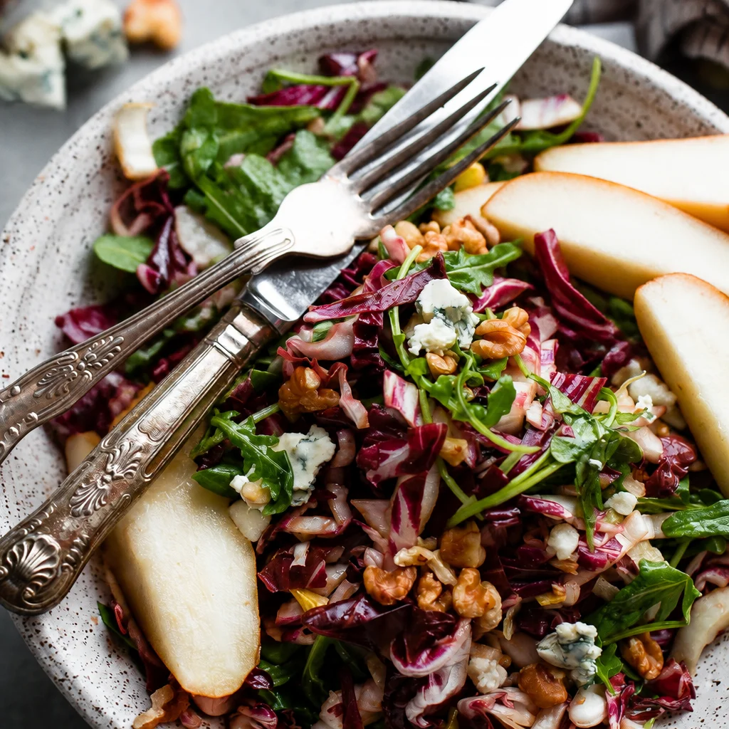 Colorful harvest salad with greens, apples, and pomegranate topped with vinaigrette.